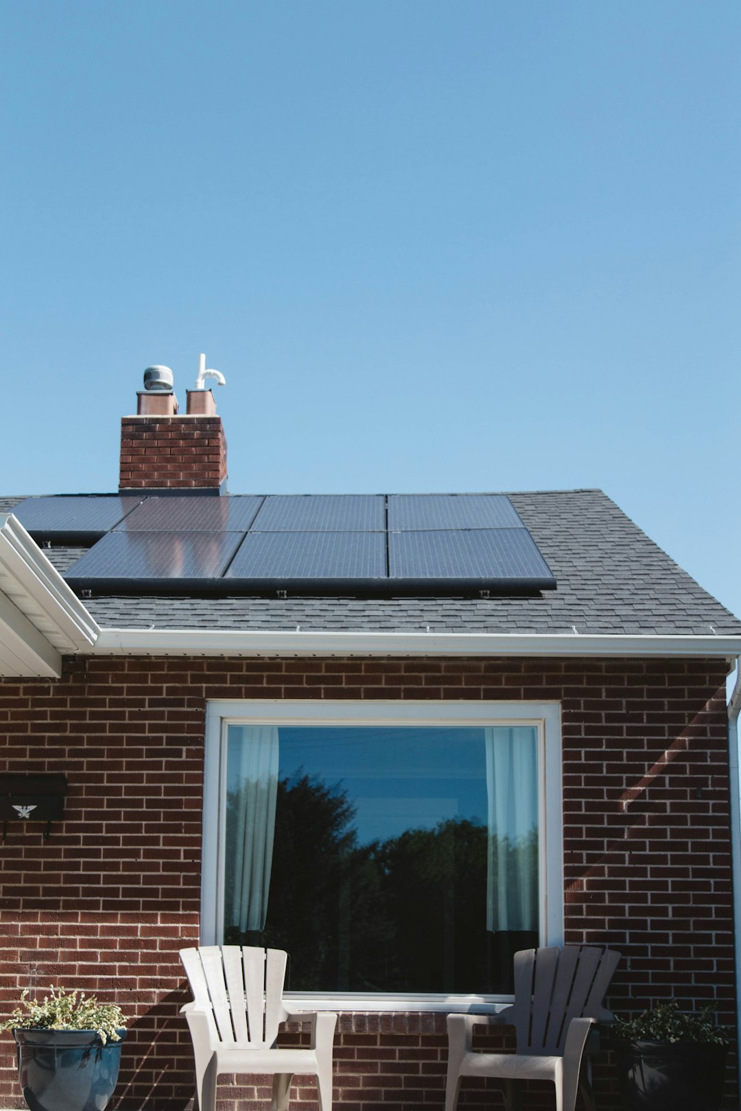 service-02 Vivint Solar - Solar Panels on roof of brick home with window and Adirondack chairs.